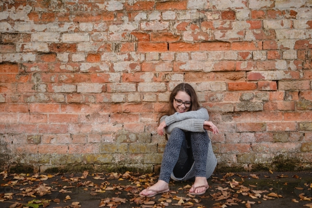 Young teenage girl leaning against red brick wall laughing - Australian Stock Image
