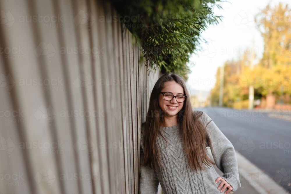 Young teenage girl leaning against timber fence with hand on hip laughing - Australian Stock Image