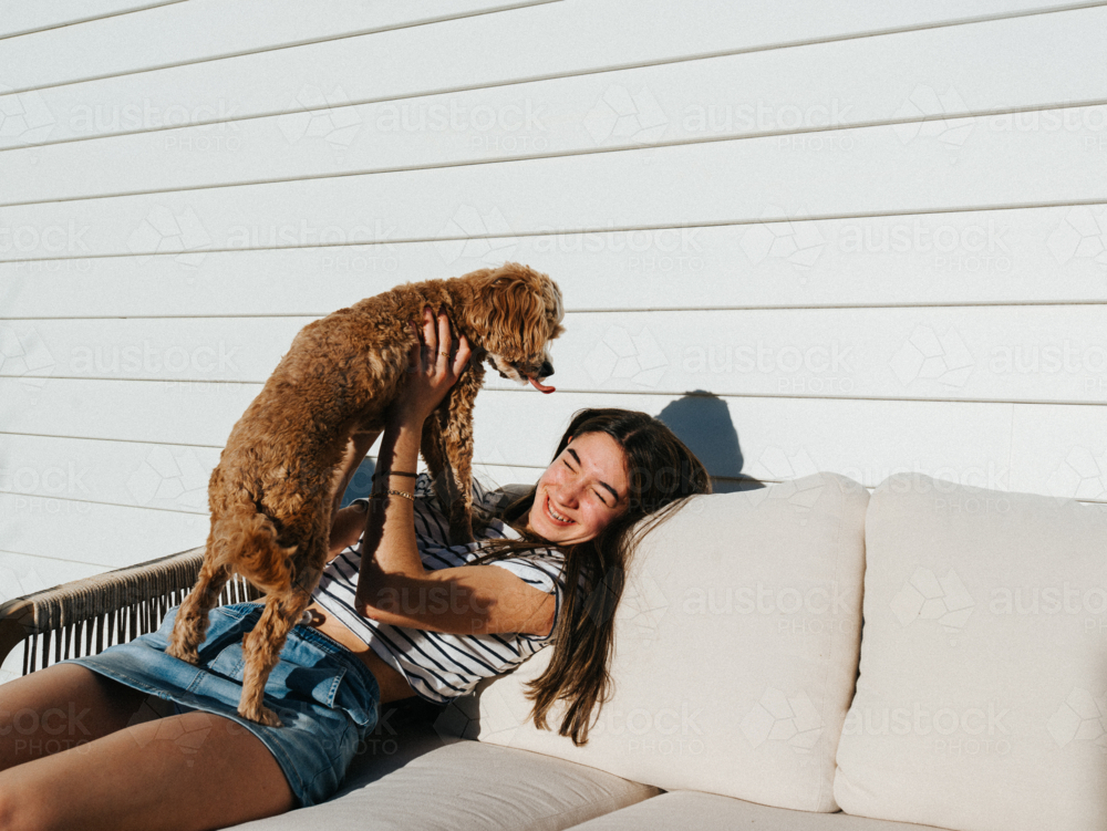 Young teenage girl playing with a small brown dog on the couch. - Australian Stock Image