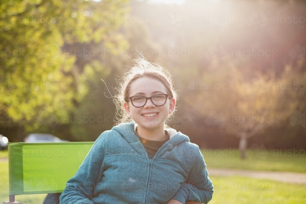 Young teenage girl sitting on outdoor chair in afternoon light - Australian Stock Image