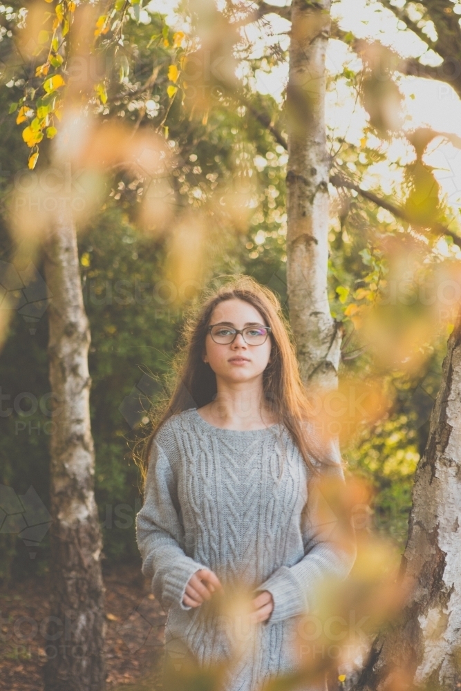 Young teenage girl standing in between trees in afternoon light - Australian Stock Image