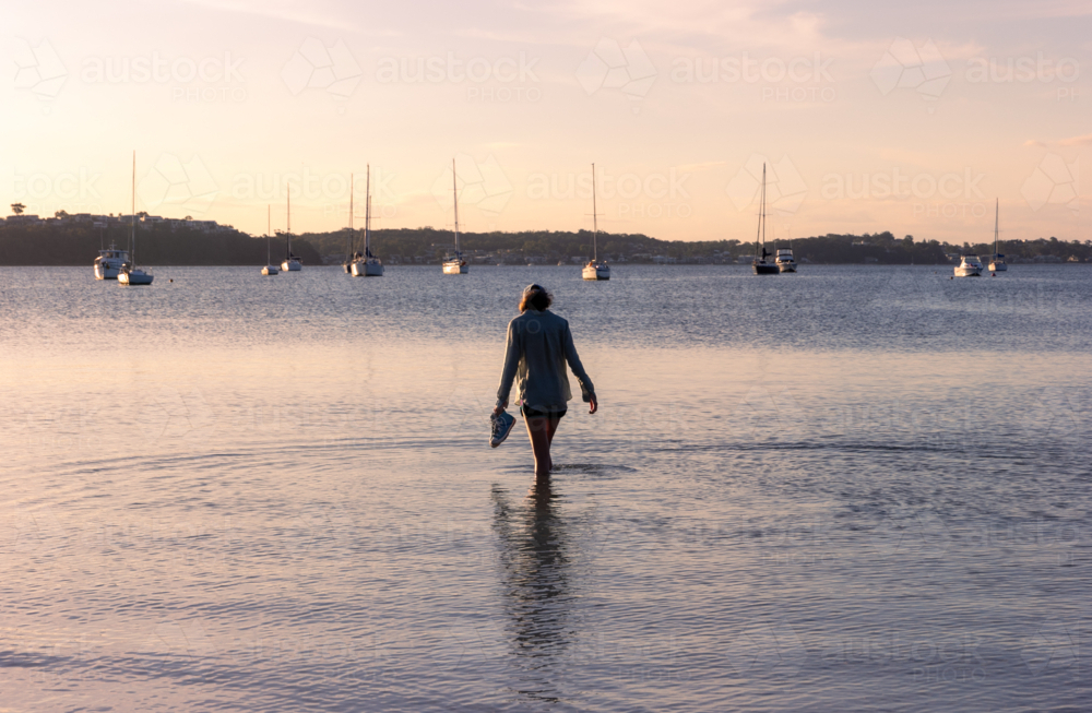 Young teenage girl standing in calm water in the late afternoon with boats in the background - Australian Stock Image