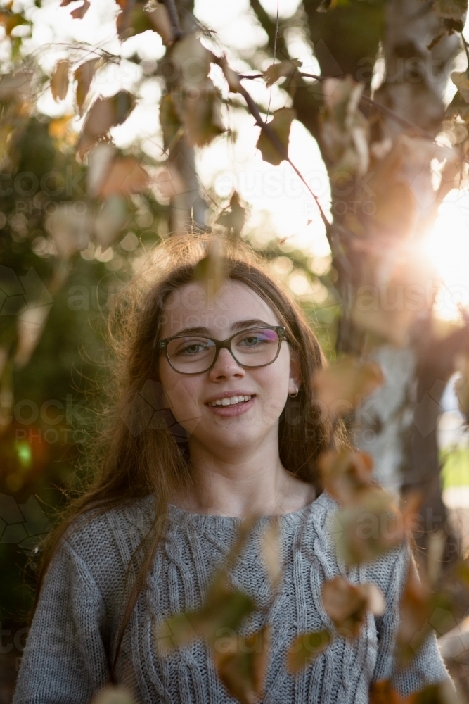 Young teenage girl standing near trees with leaves framing the image - Australian Stock Image