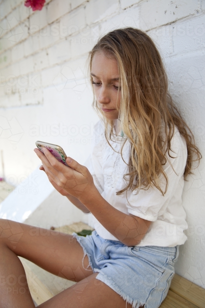 Young teenager sitting on a bench looking at her phone - Australian Stock Image