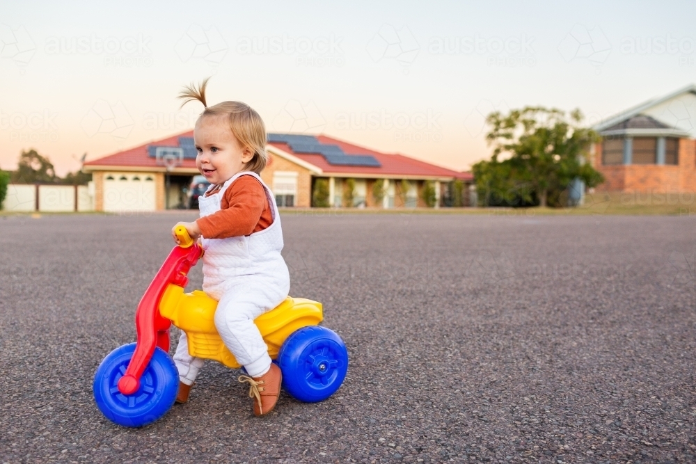Young toddler kid riding past houses on quiet urban street at dusk - Australian Stock Image