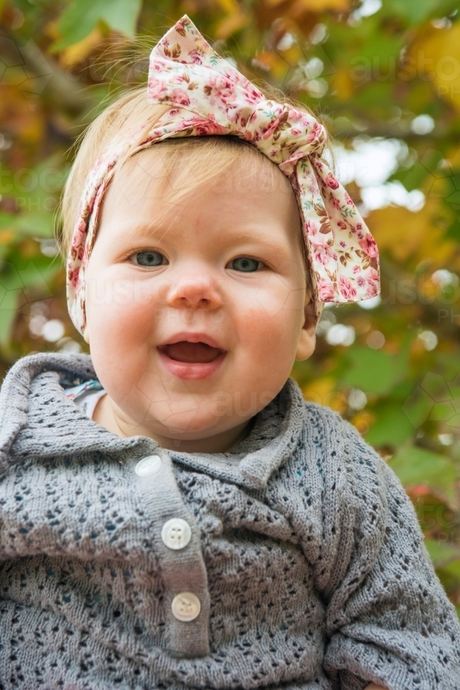 Young toddler looking at camera against background of autumn leaves - Australian Stock Image