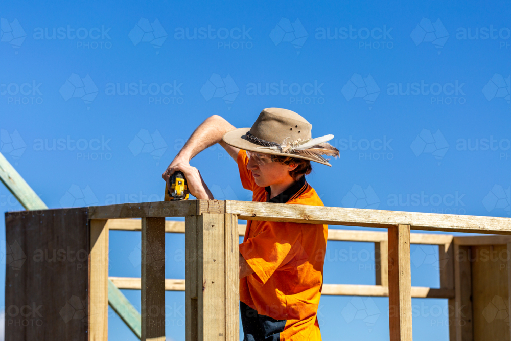 Young trainee trade apprentice building frame in bright sunlight against blue Australian sky - Australian Stock Image