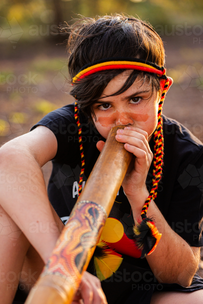 Young tween Aboriginal boy outside in rural Australia playing didgeridoo - Australian Stock Image