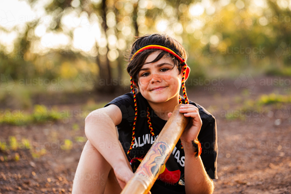 Young tween Aboriginal boy portrait outside in rural Australia with didgeridoo smiling - Australian Stock Image