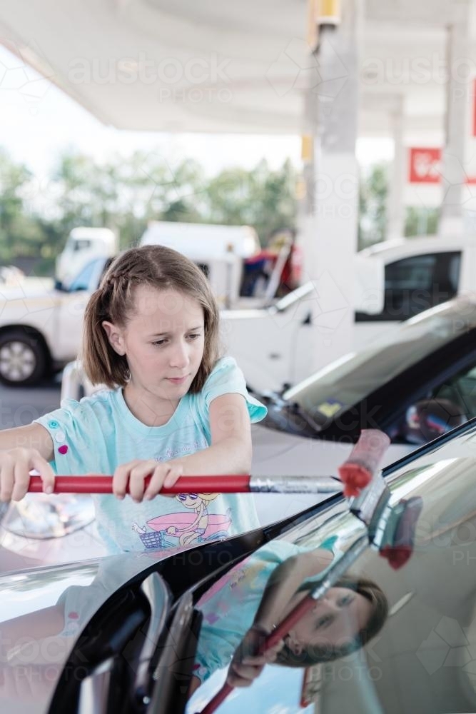 Young tween girl cleaning the windscreen of a car - Australian Stock Image