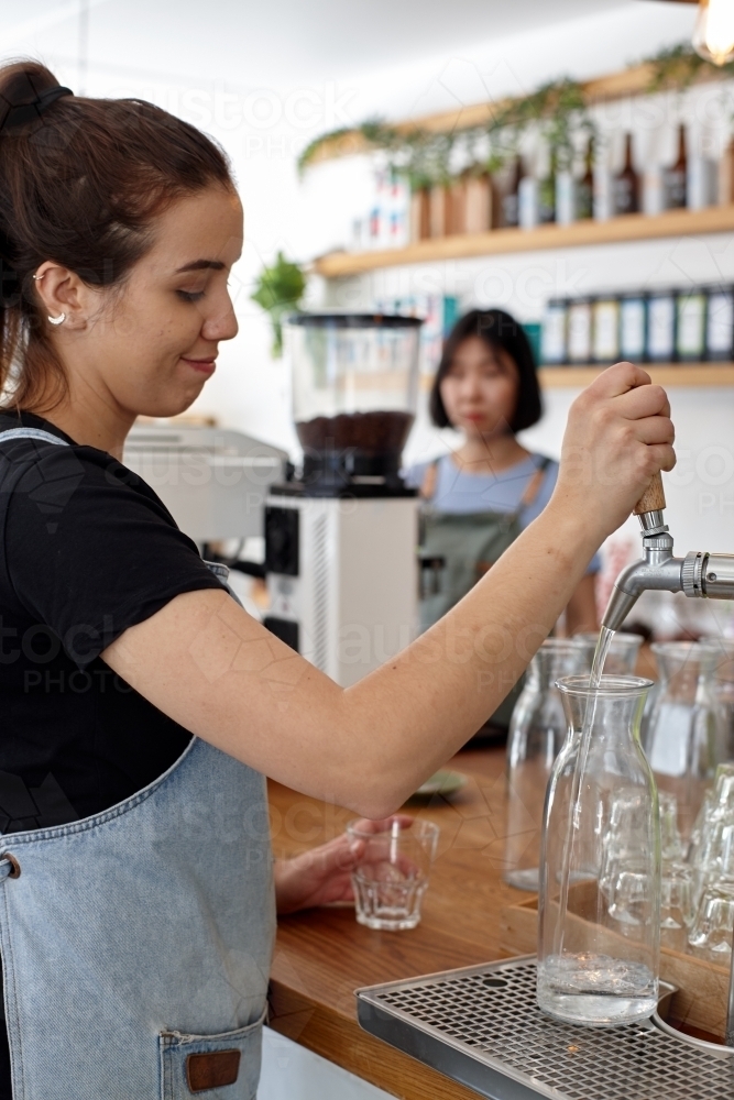 Young waiter serving water at cafe - Australian Stock Image