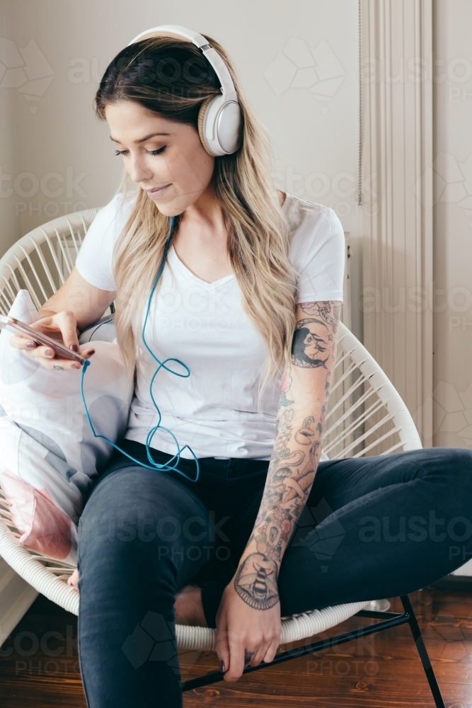Young woman at home with headphones connected to her smartphone : Austockphoto Young woman at home with headphones connected to her smartphone - Australian Stock Image