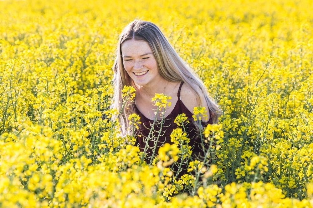 Young woman bent over laughing on farm in field of canola flowers - Australian Stock Image