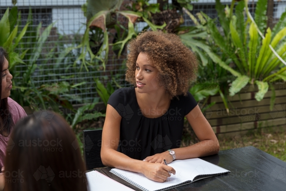 Young woman collaborating outside at a table with colleagues - Australian Stock Image