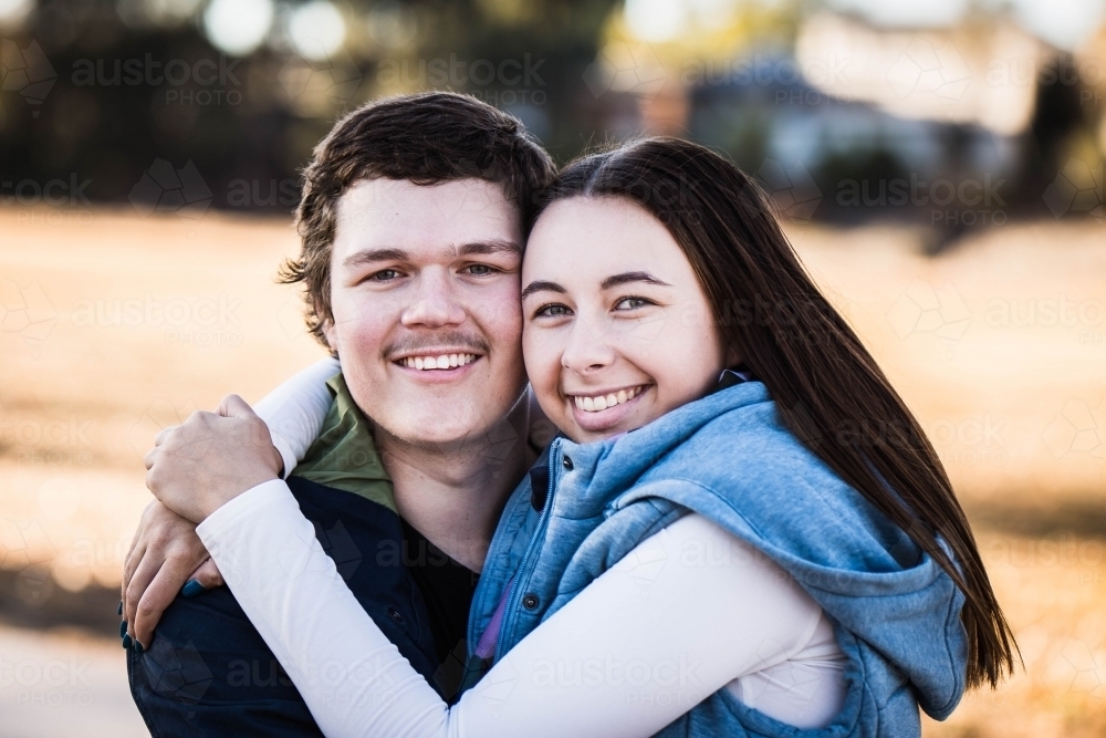 Young woman cuddling boyfriend smiling - Australian Stock Image