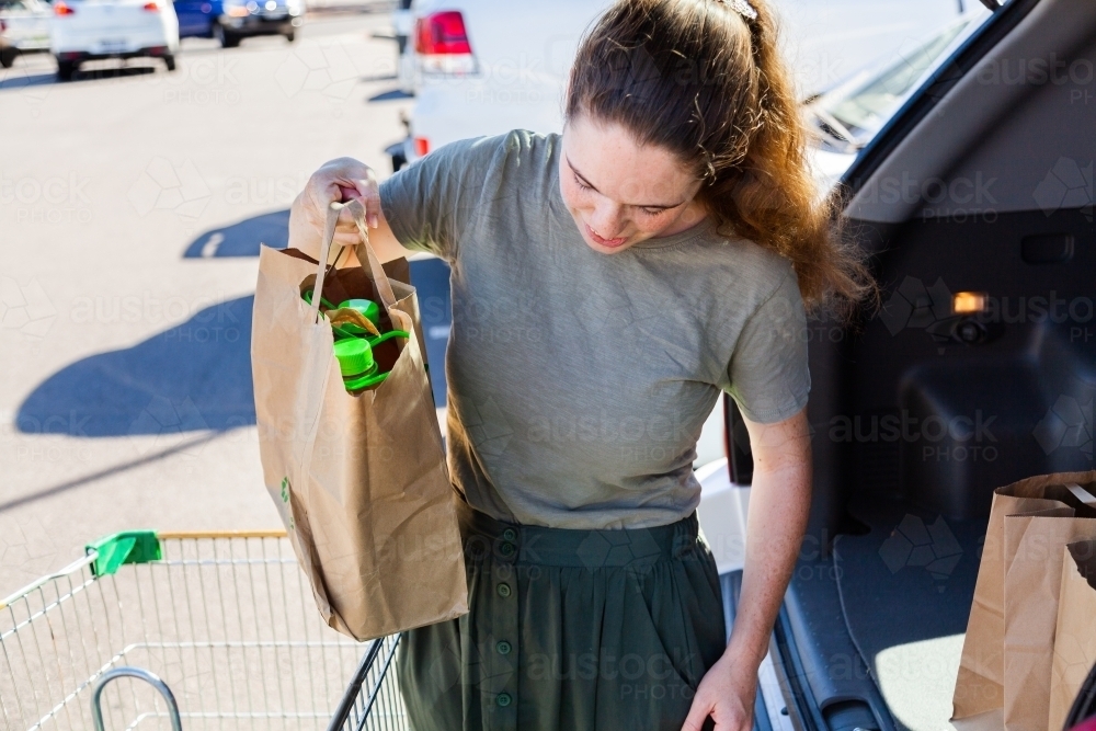 Young woman doing the shopping and loading paper bags into car from click and collect order - Australian Stock Image