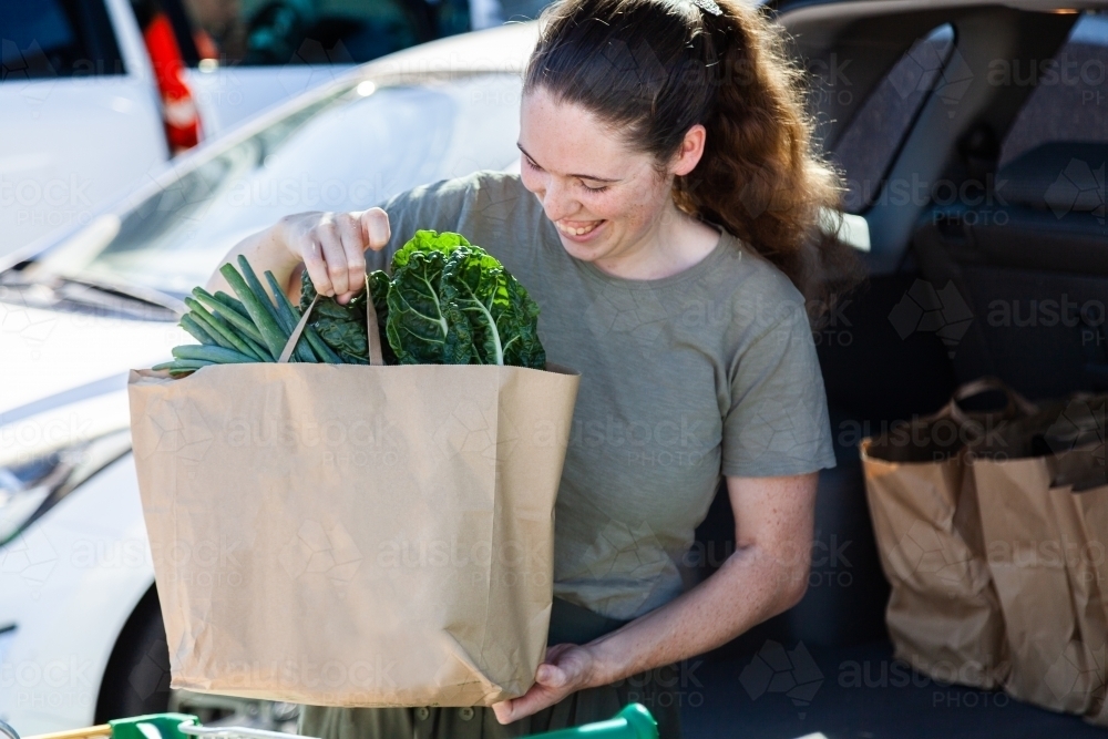 Young woman doing the shopping and loading paper bags into car from click and collect order - Australian Stock Image