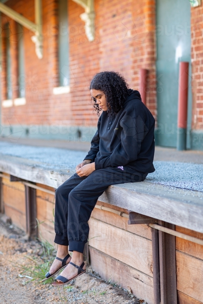 young woman dressed in black sitting on abandoned station platform - Australian Stock Image
