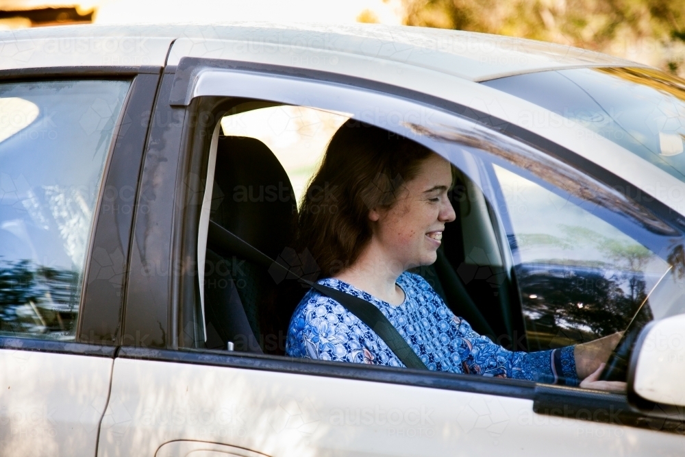 Young woman driving white car and smiling with window down - Australian Stock Image