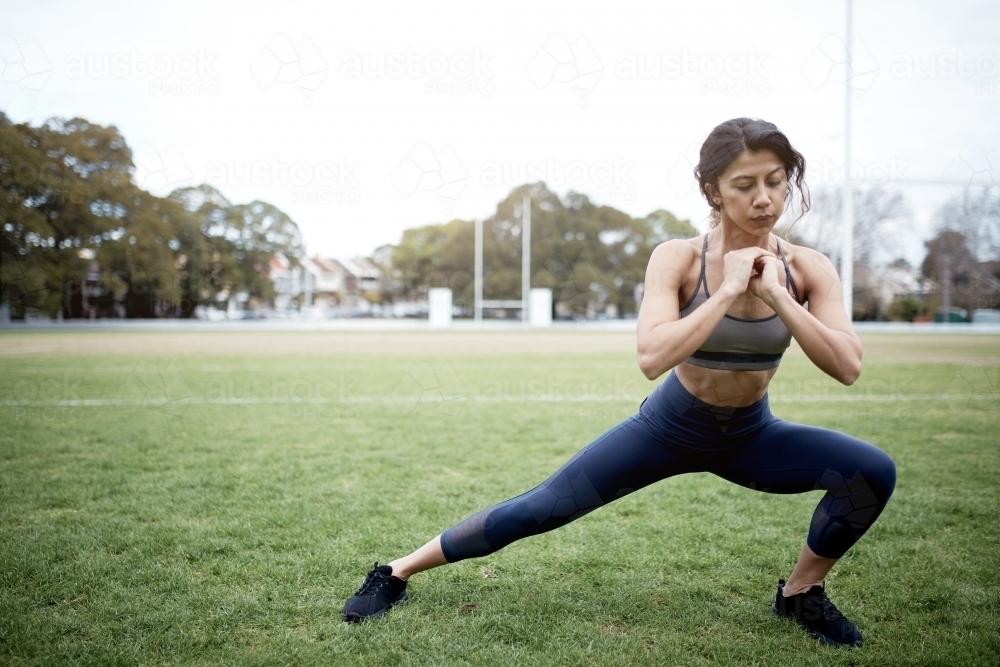 Young woman fitness training at oval doing squats - Australian Stock Image