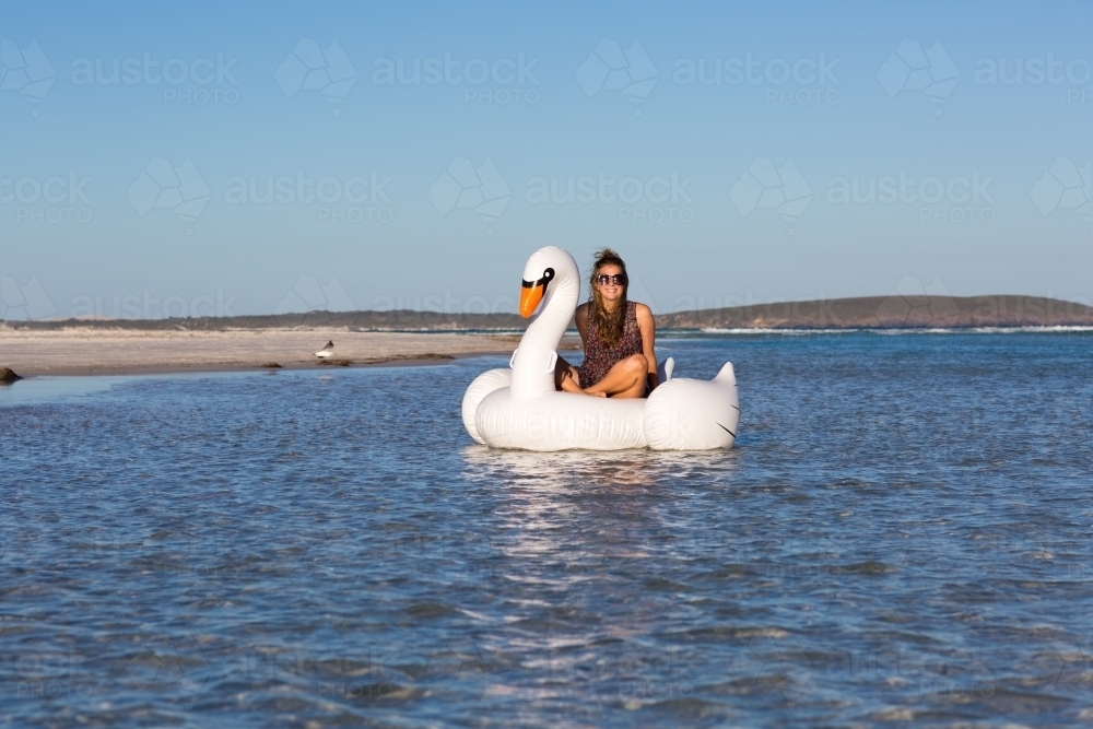 Young woman floating in a white inflatable swan - Australian Stock Image