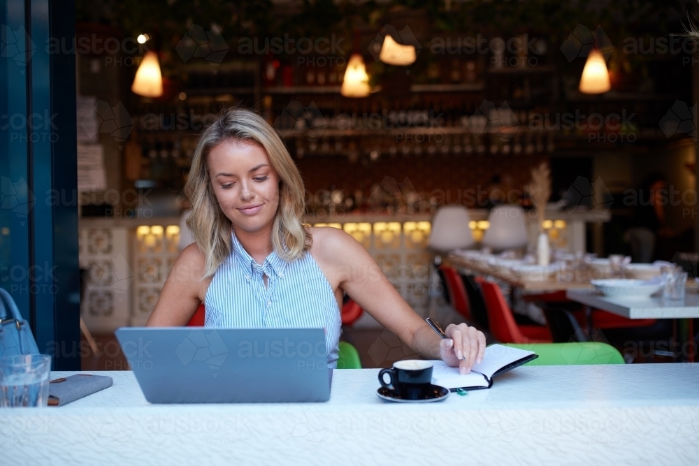 Young woman freelancing from her laptop at cafe - Australian Stock Image