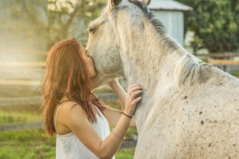 Young woman giving her grey horse a kiss - Australian Stock Image