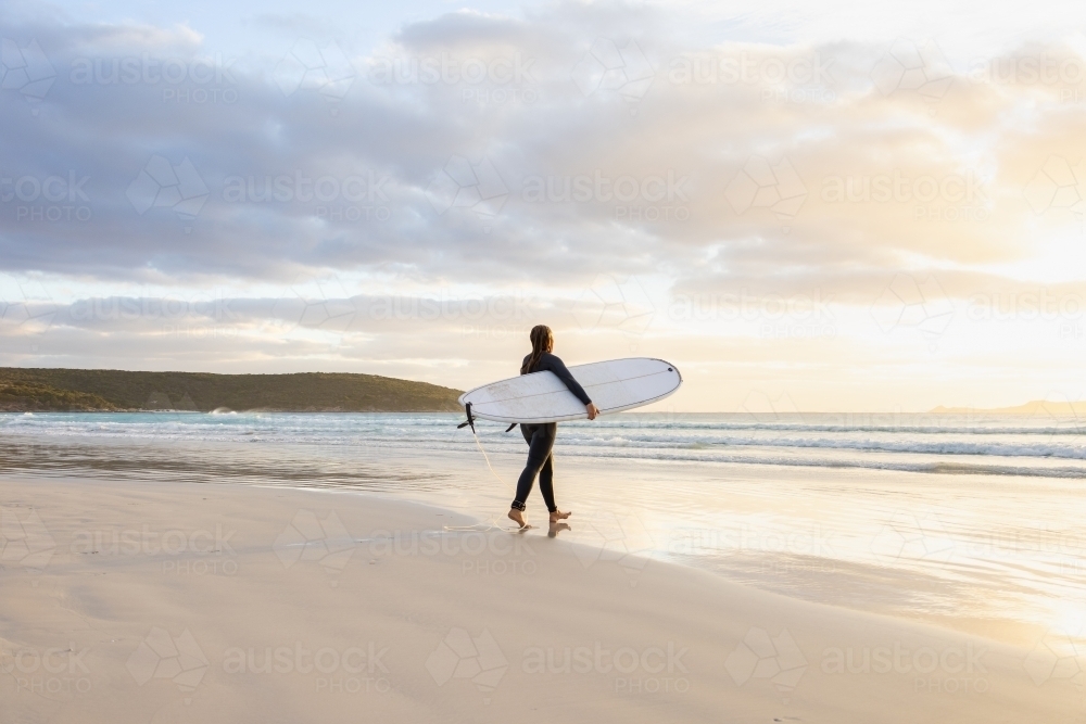 young woman heading into the surf carrying long board - Australian Stock Image