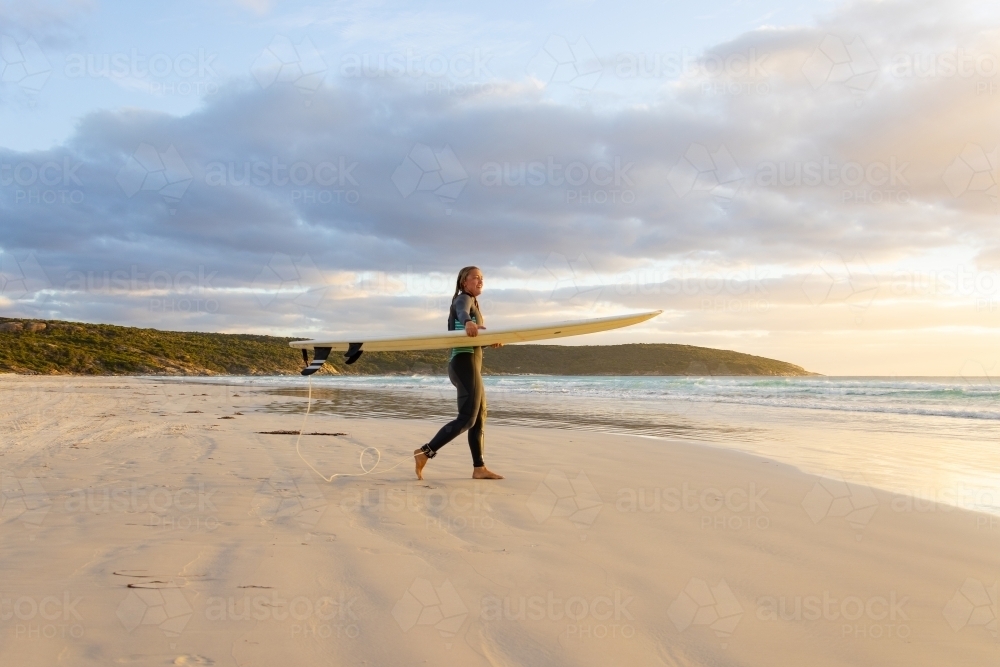 young woman heading into the surf carrying long board - Australian Stock Image