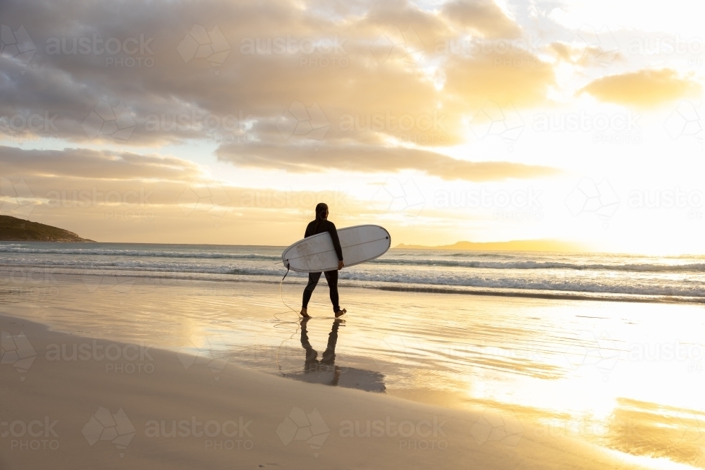 young woman heading into the surf carrying long board - Australian Stock Image