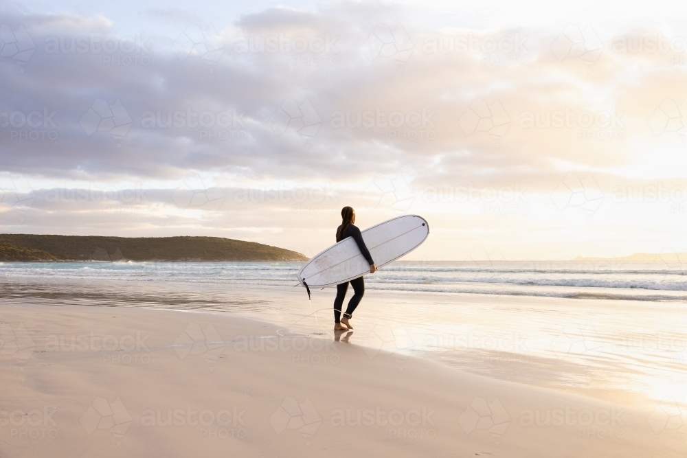 young woman heading into the surf carrying long board - Australian Stock Image