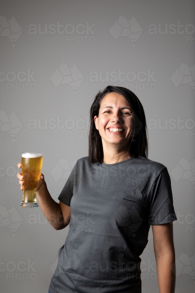 Young woman holding a glass of beer, relaxed and happy - Australian Stock Image