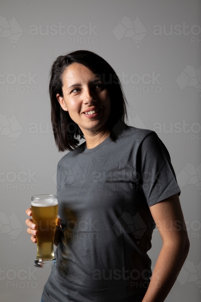 Young woman holding a glass of beer, relaxed and happy - Australian Stock Image
