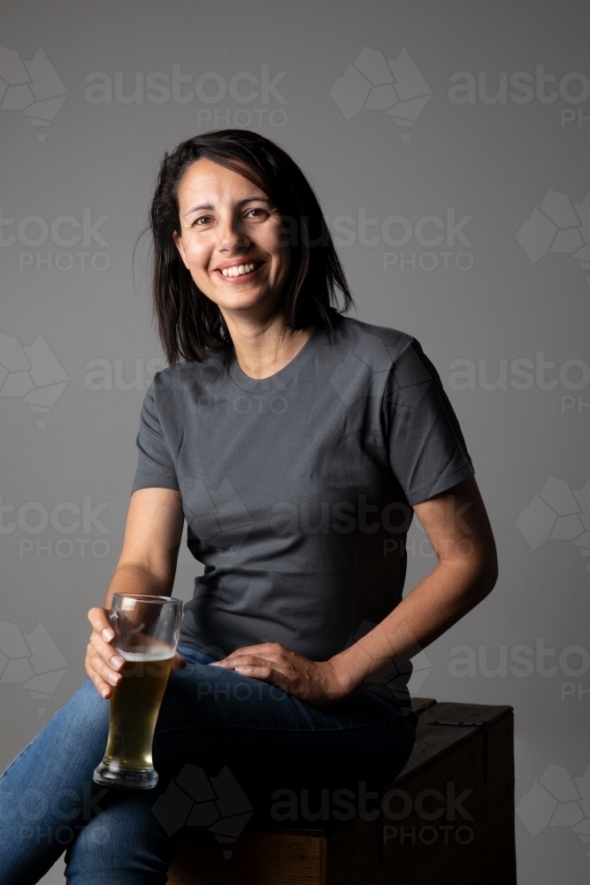 Young woman holding a glass of beer, relaxed and happy - Australian Stock Image