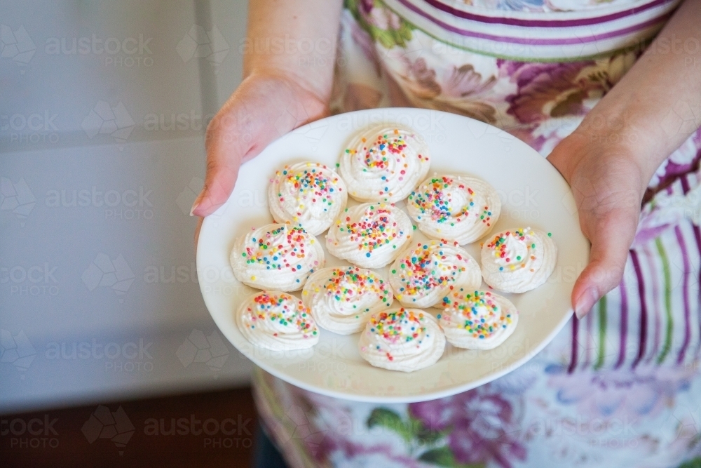 Young woman holding a plate of meringues with sprinkles - Australian Stock Image