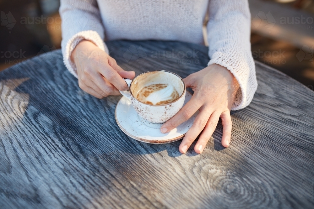 Young woman holding cup of coffee on wooden table in the morning - Australian Stock Image