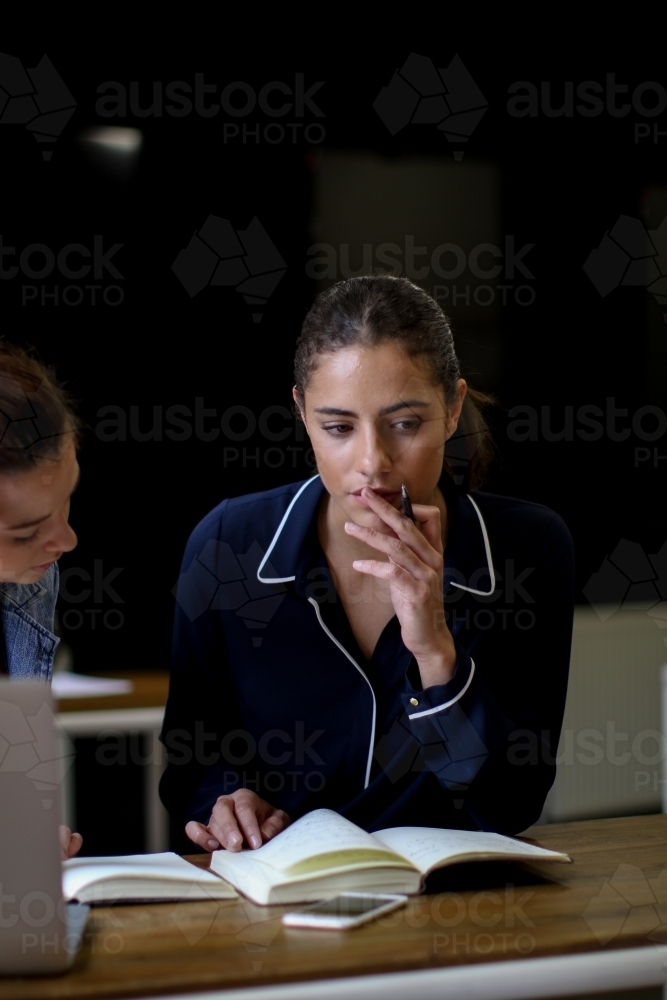 Young woman holding pen looking over notes with thoughtful expression - Australian Stock Image