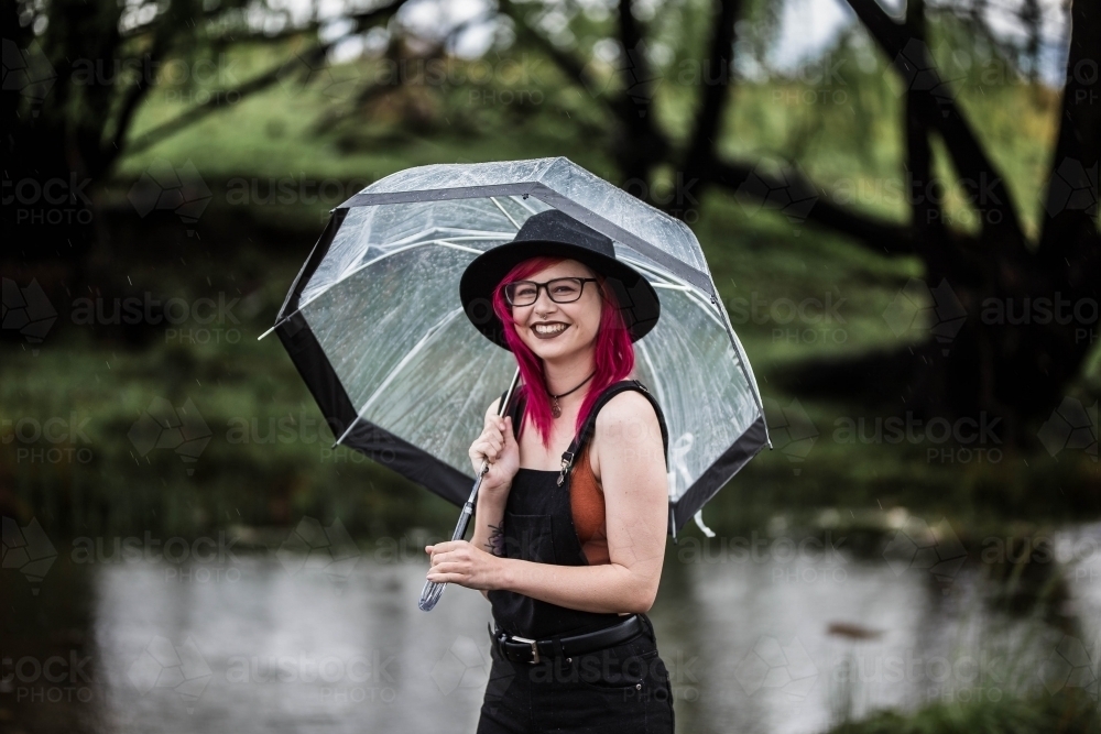 Young woman in 20s holding umbrella in rain laughing - Australian Stock Image
