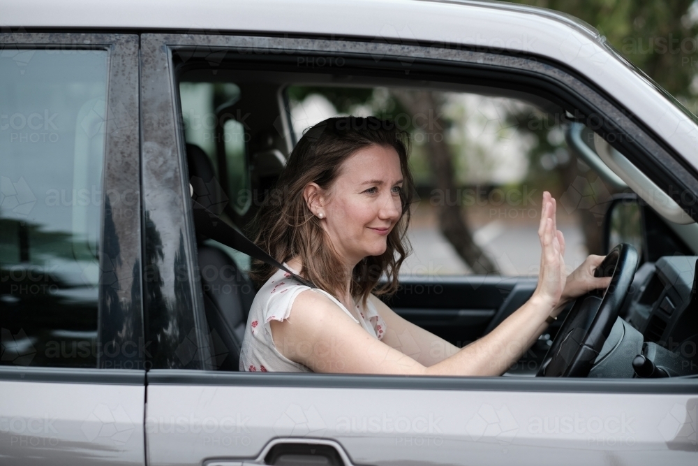 Young woman in 4wd vehicle thanking another driver by waving - Australian Stock Image
