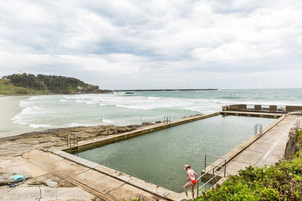 Young woman in bikini stepping into ocean bath on beach - Australian Stock Image