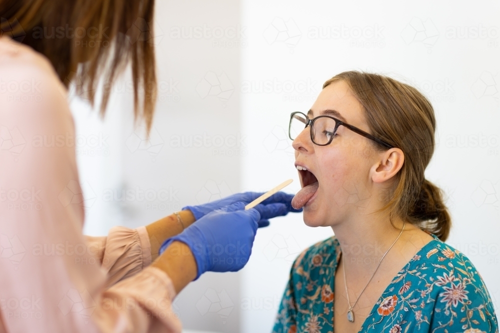young woman in doctors surgery with doctor checking throat - Australian Stock Image