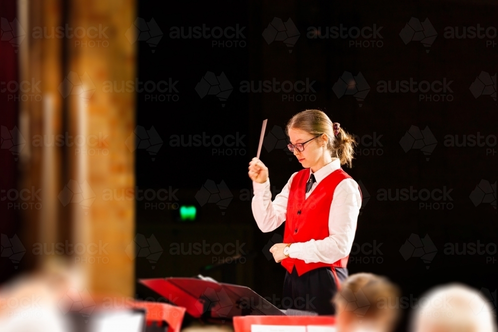 Young woman in her twenties conducting a band performing on stage at concert - Australian Stock Image