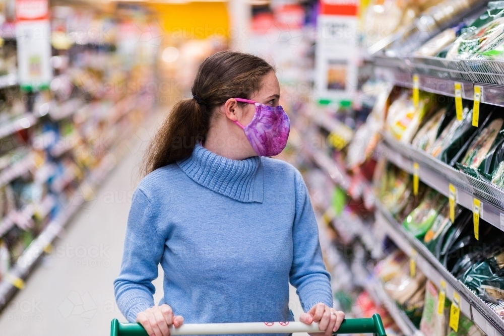 Young woman in her twenties wearing a face mask in shopping aisle, choosing what to buy - Australian Stock Image