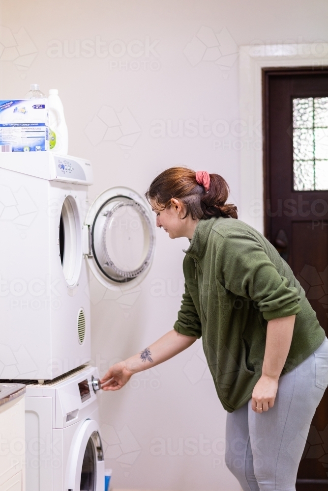 young woman in laundry turning on washing machine - Australian Stock Image