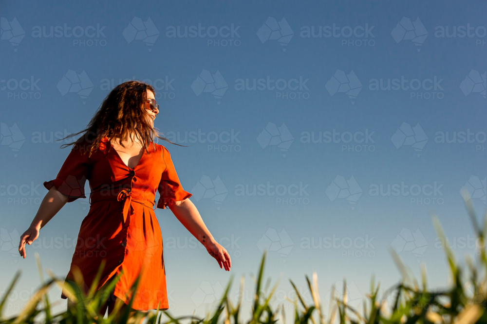 Young woman in red dress twirling in a green field - Australian Stock Image