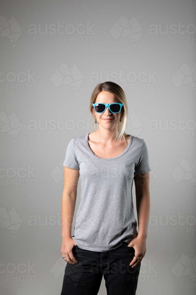 Young woman in relaxed pose wearing casual gear, blue sunglasses - Australian Stock Image