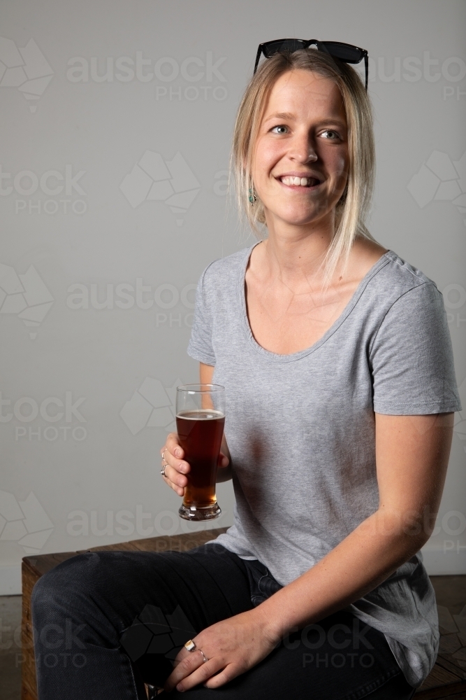 Young woman in relaxed pose wearing casual gear, holding a beer - Australian Stock Image