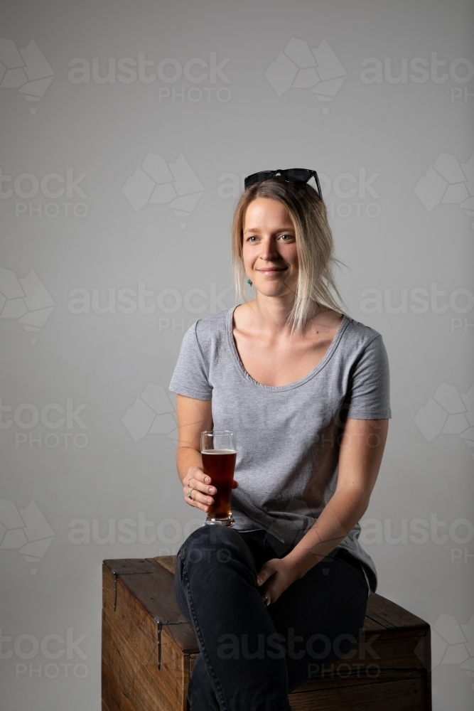 Young woman in relaxed pose wearing casual gear, holding a glass of beer - Australian Stock Image