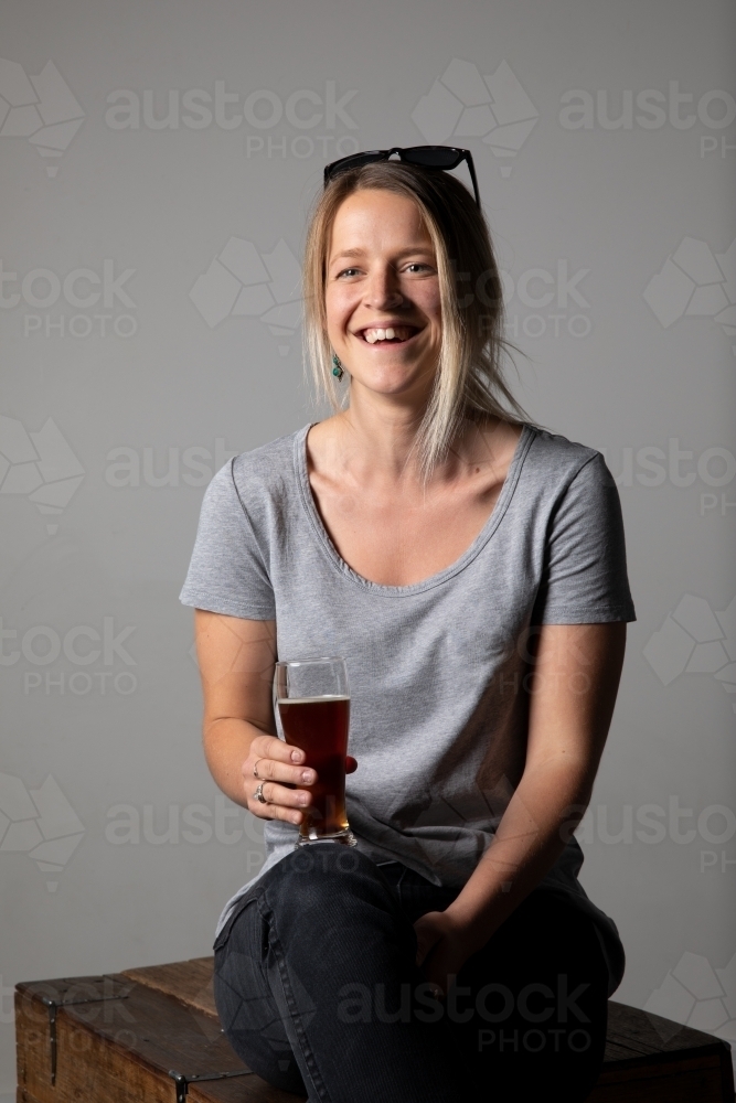 Young woman in relaxed pose wearing casual gear, holding a glass of beer - Australian Stock Image