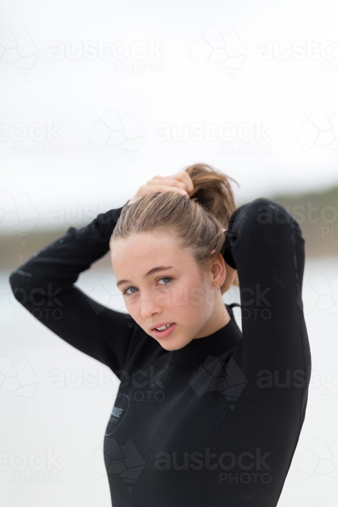 Young woman in wetsuit tying hair back - Australian Stock Image